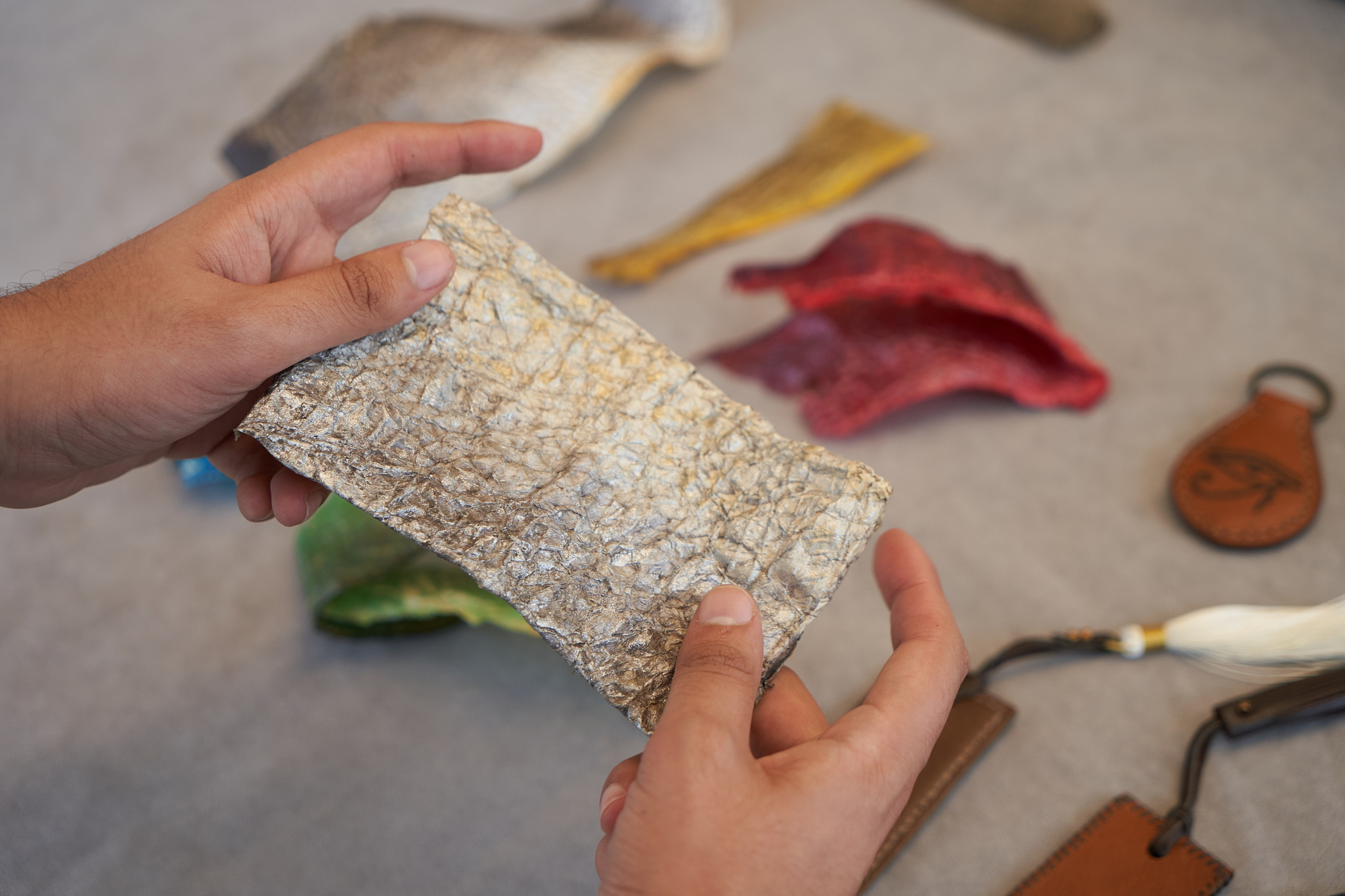 Hands holding a textured fish skin material sample beside colour studies